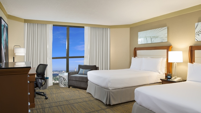 A hotel room featuring 2 freshly made beds and a view of the blue sky over Miami.