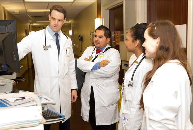 Dr. Swords and lab technicians view a computer on a rolling cart