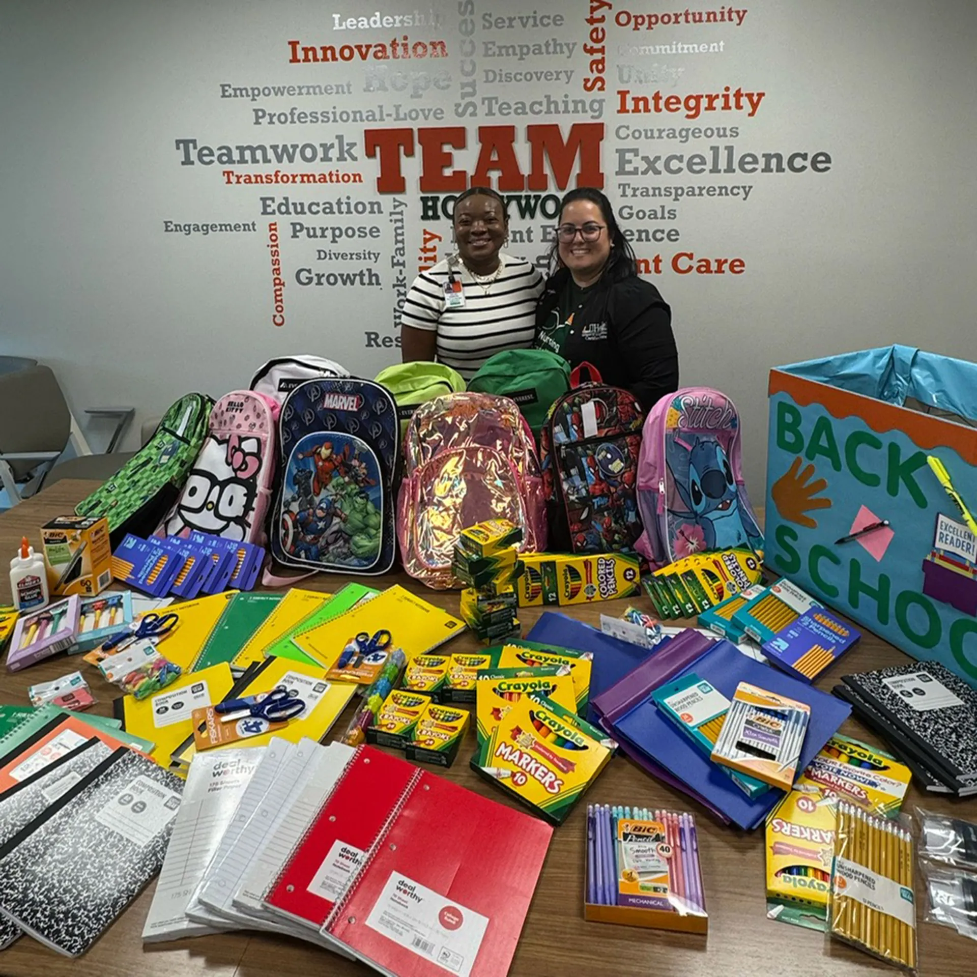 Two nurses pose with school supplies and back packs