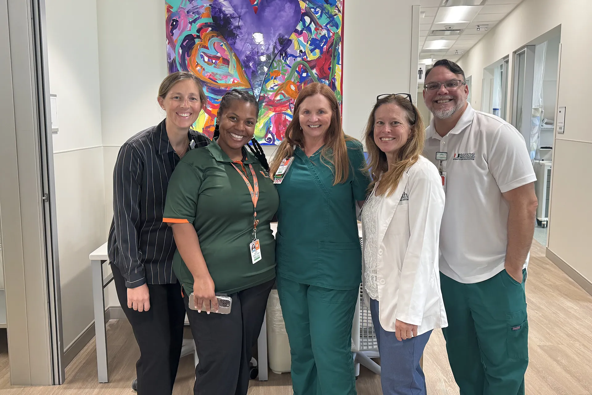 Nurses take a group picture in a hallway with colorful art piece in the background