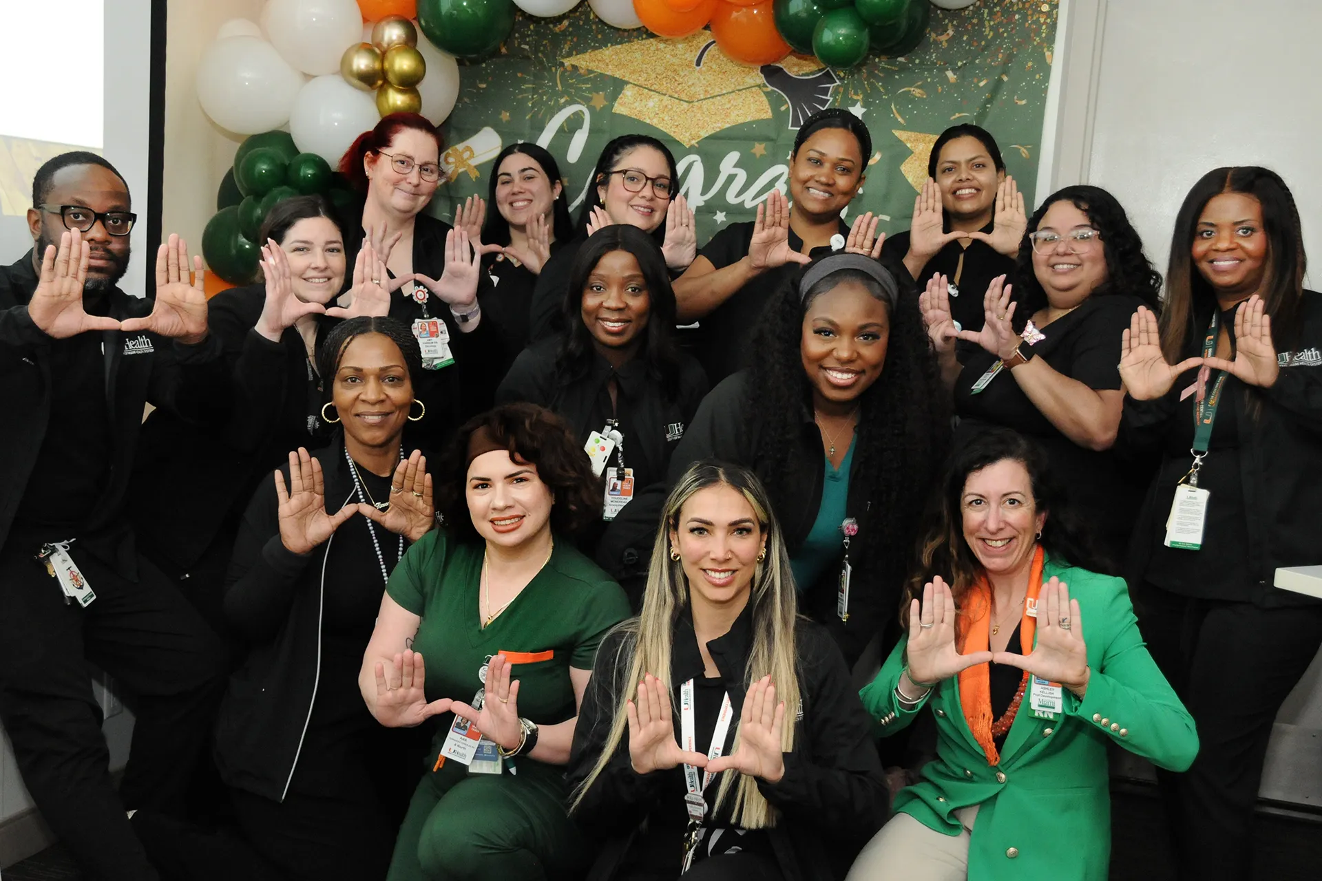 Group of nurses wearing black and green scrubs pose for a photo