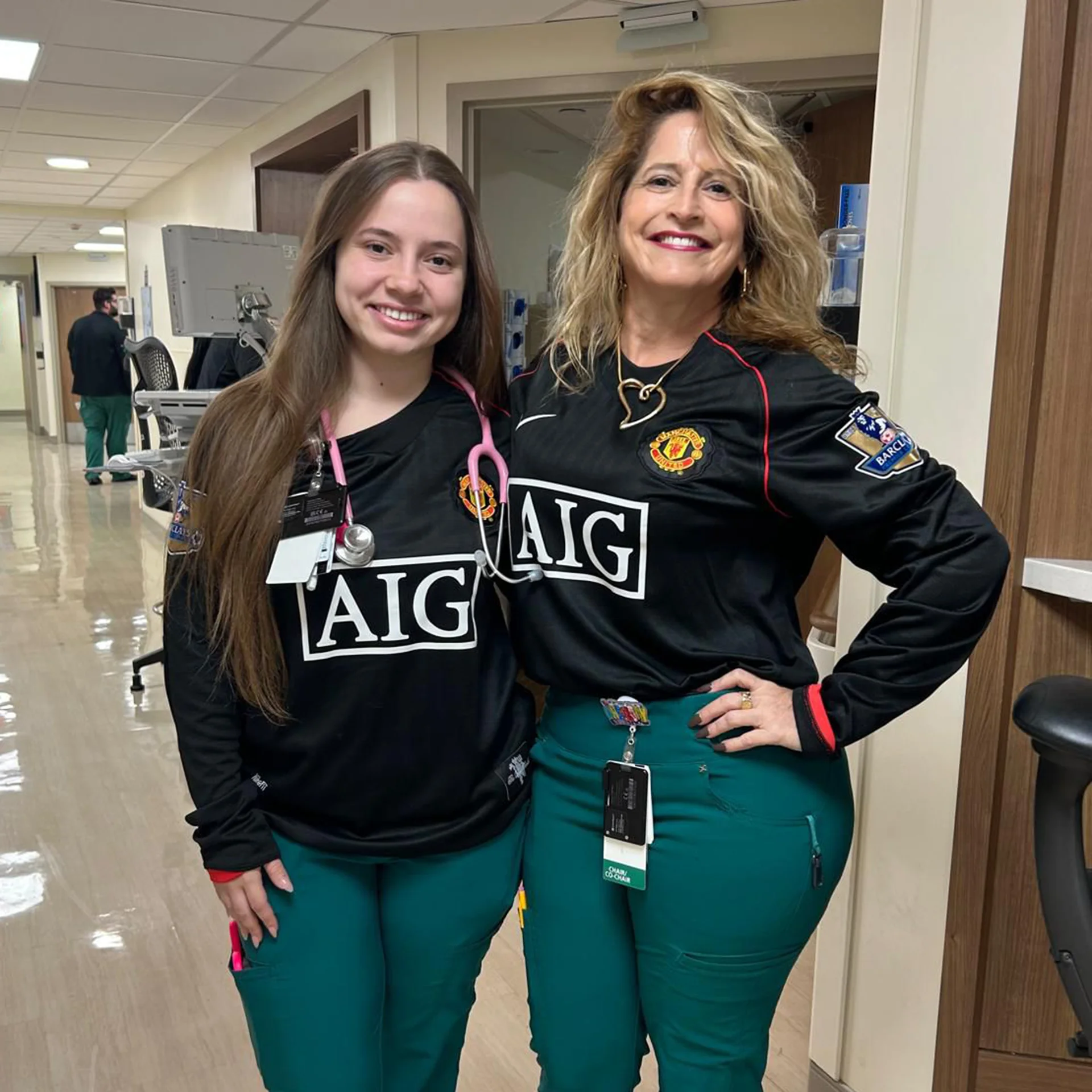 Two women in scrubs pose for a photo inside a hospital