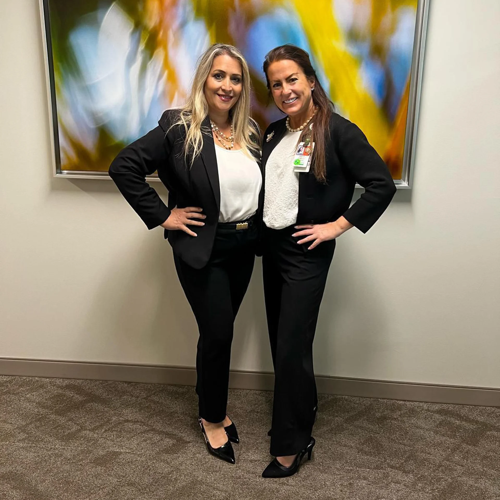 Two women pose in front of colorful art piece