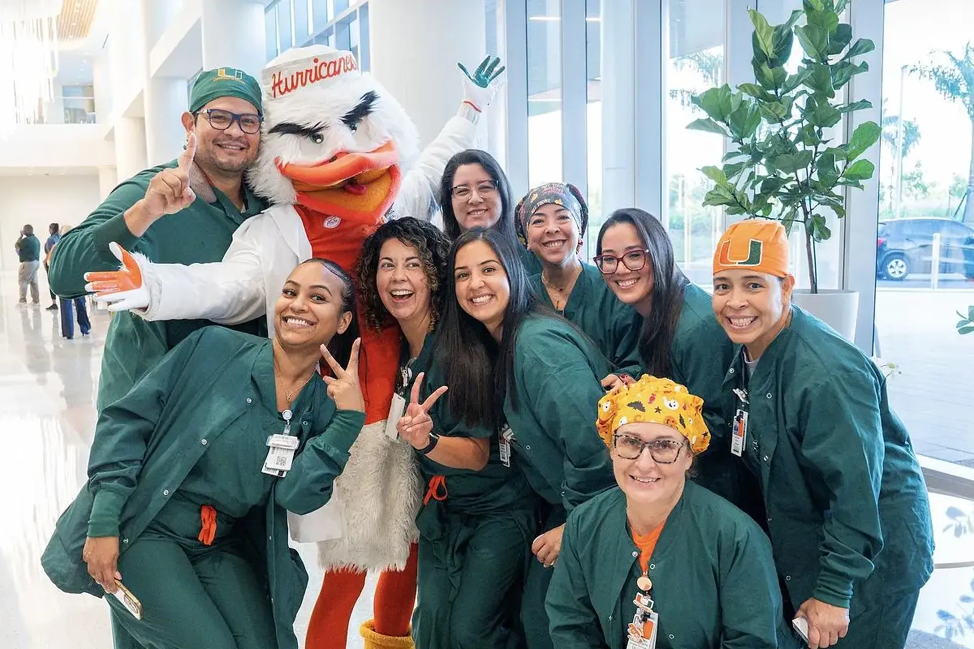 Group of nurses in green scrubs pose for a group photo with Sebastian the Ibis